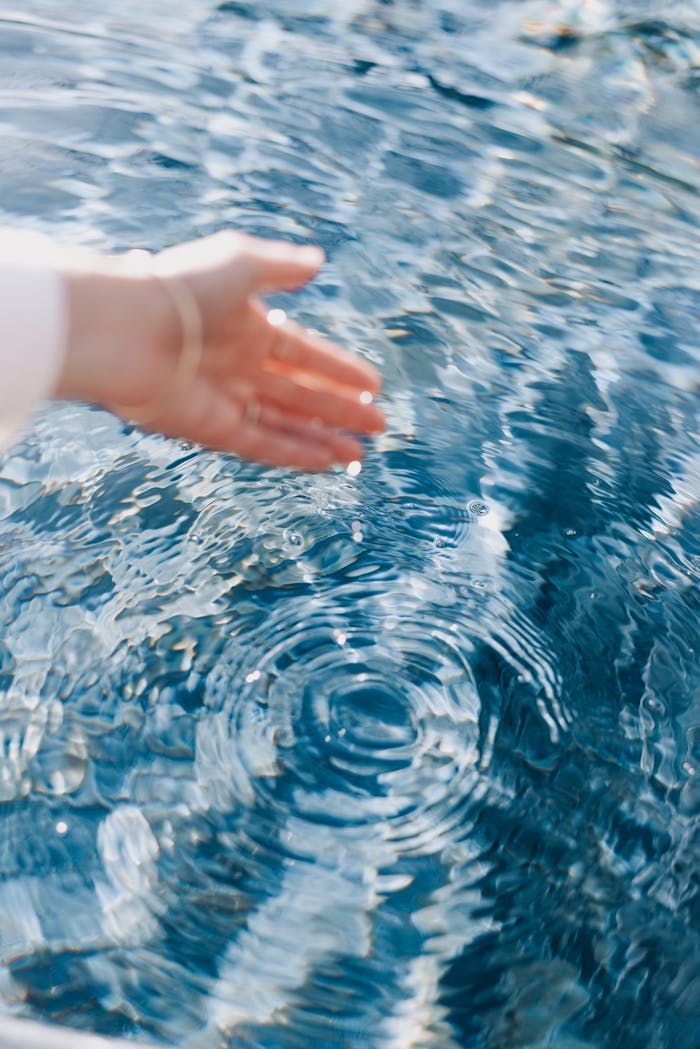 A close-up of a hand touching clear blue water creating beautiful ripples, evoking a sense of tranquility.