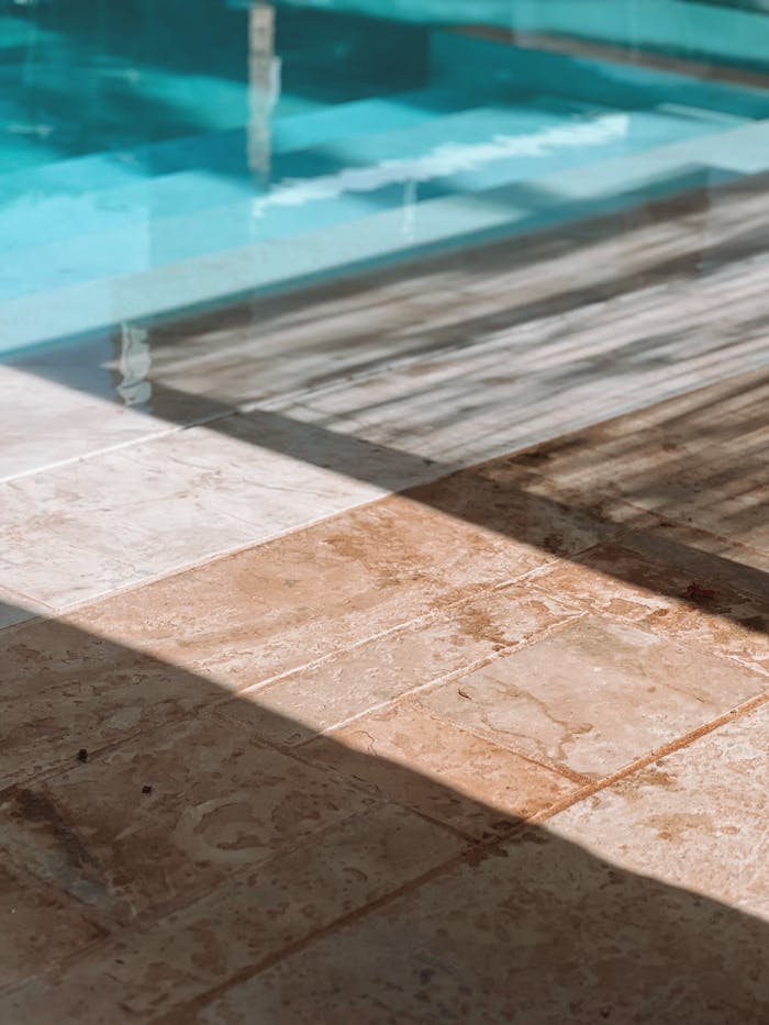 A serene close-up of sunny poolside with clean marble tiles and intriguing shadows.